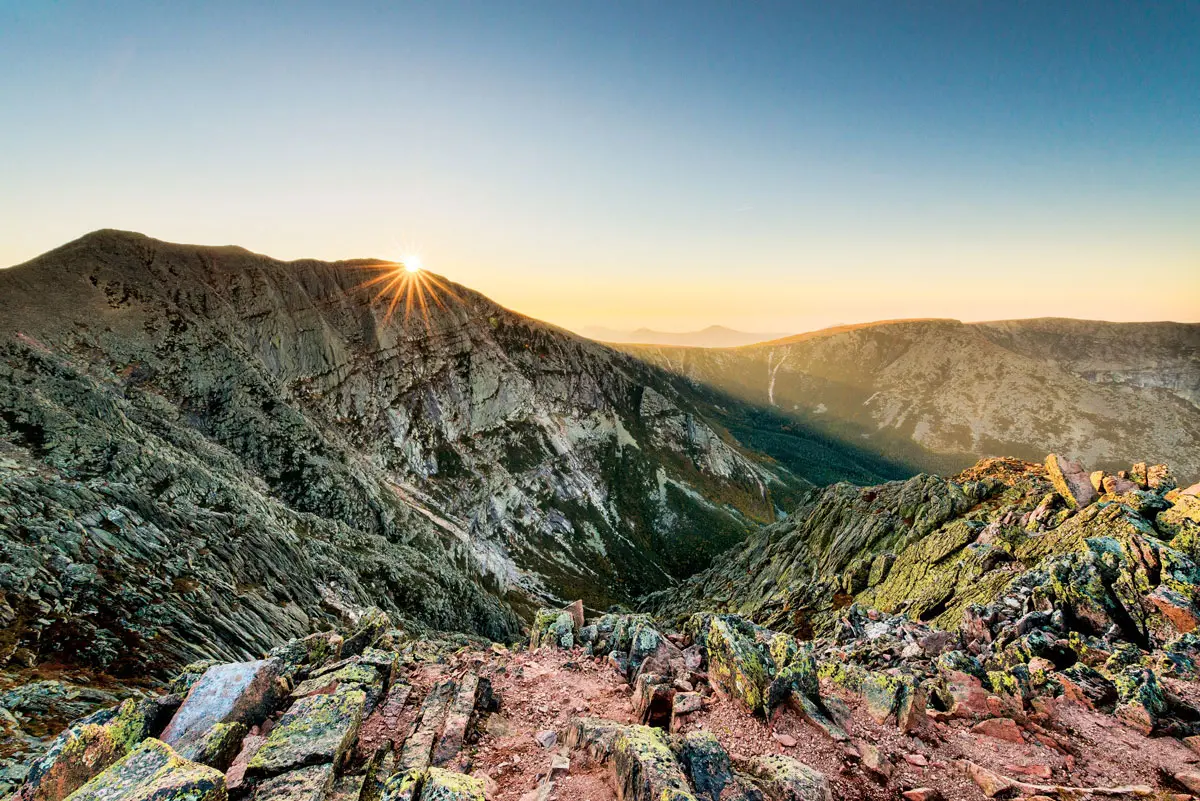The sun is setting over the Baxter State Park mountain range.