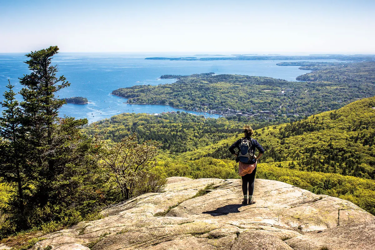 A woman standing on a rock formation and overlooking the landscape at Camden Hills State Park.
