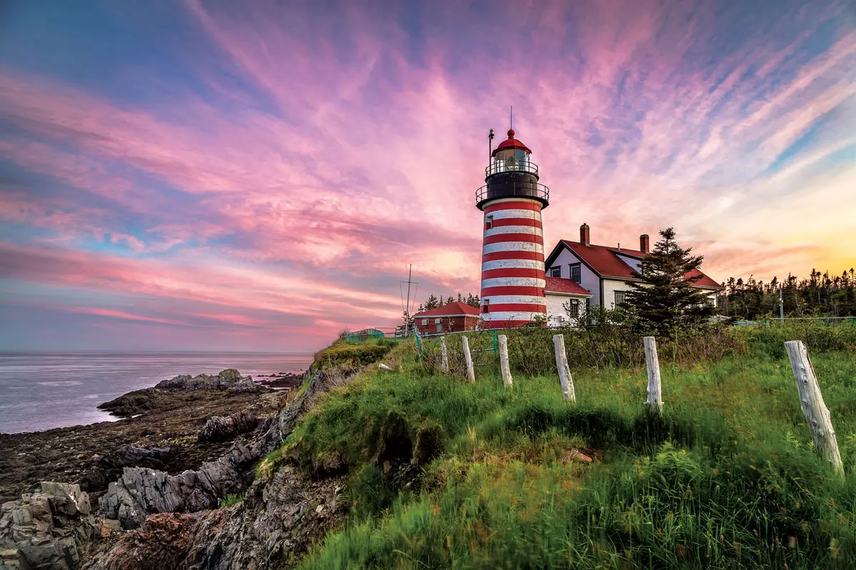 A red and white light house sitting on top of Quoddy Head State Park's lush green hillside.	