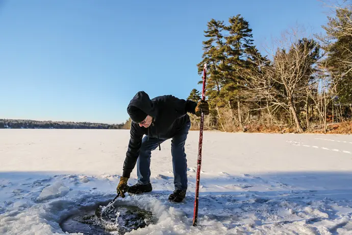 Laukka skims away ice after cutting a hole for plunging in Crawford Pond.