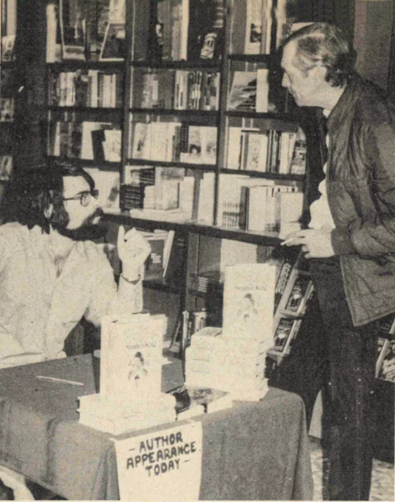 Stephen King at
a book signing, with stacks of his best sellers.