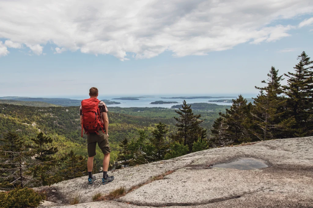 a hiker looking out to sea from atop Mansell Mountain in Acadia National Park