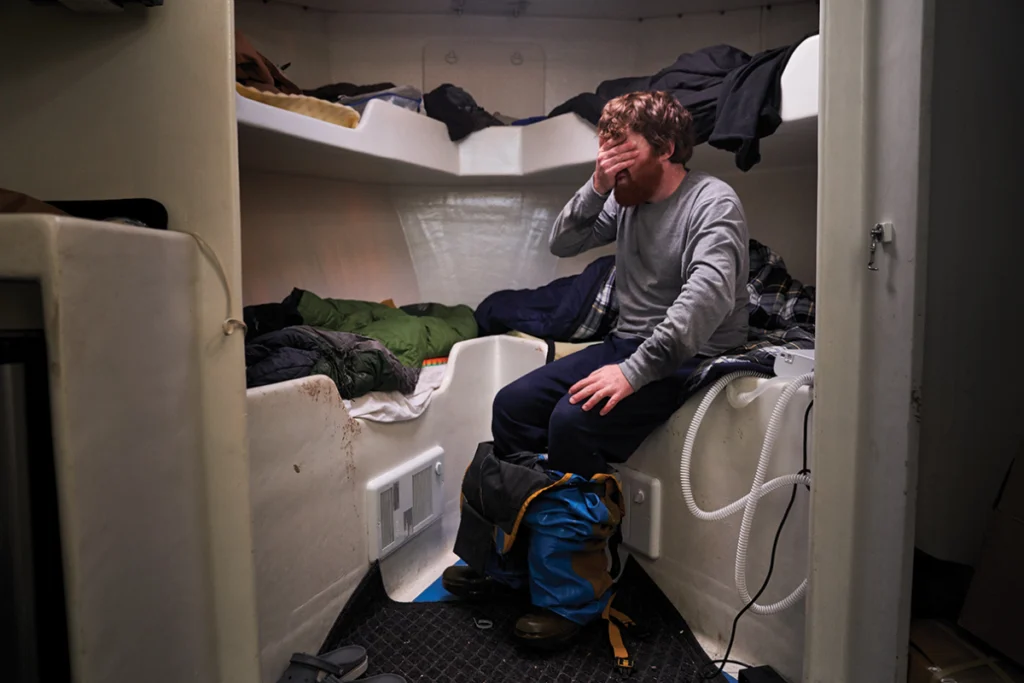 Mitchell Carney, his fishing bibs around his feet, rubs his face in exhaustion during a 10-minute lunch break