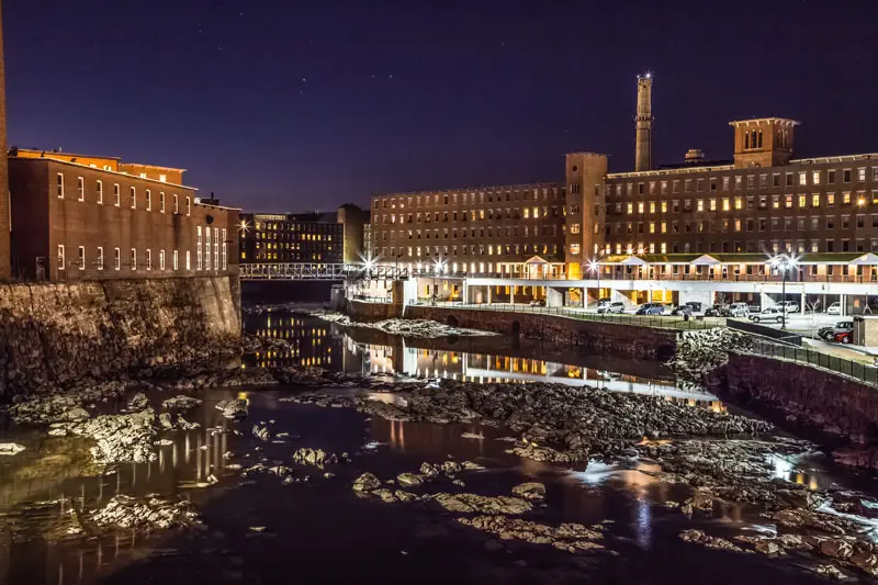 A river running through Biddeford, Maine next to tall buildings.	