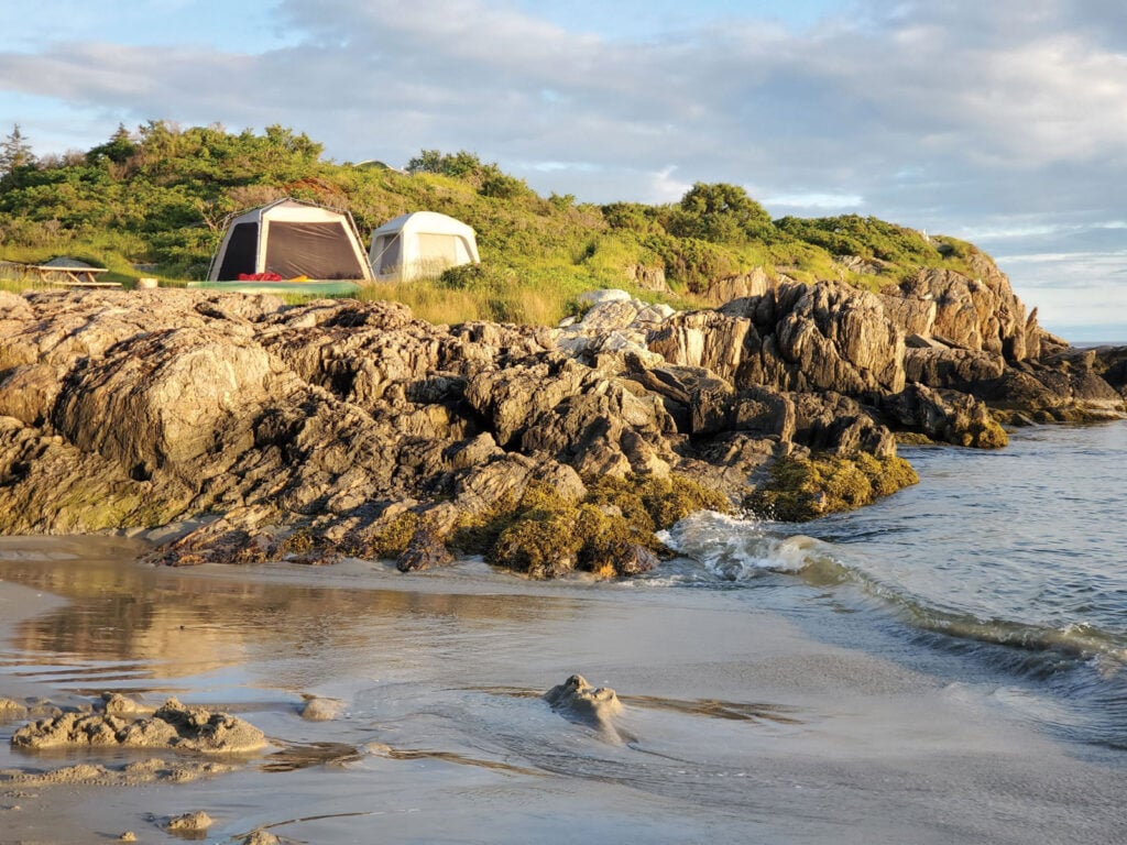 A tent on a rocky shore next to a body of water at Hermit Island Campground