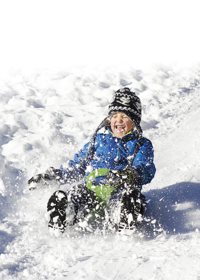 young boy in blue jacket sledding