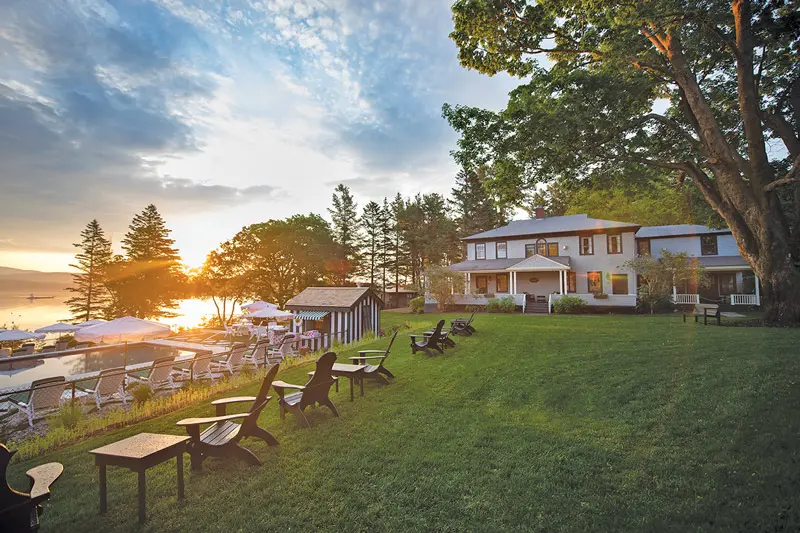 A group of benches sitting on top of a lush green field at the Claremont hotel. 