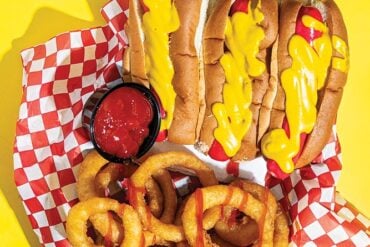 red hot dogs slathered i mustard, with onion rings drizzled with ketchup