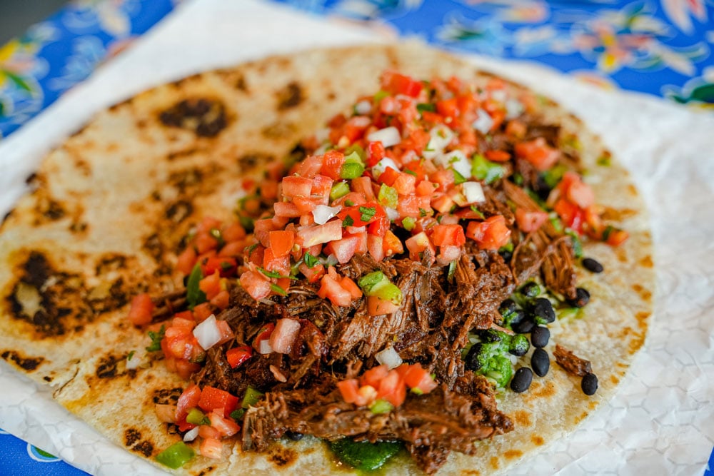 an open-faced burrito made with shredded smoked meat, rice, black beans, guacamole, and salsa from Bub’s Burritos