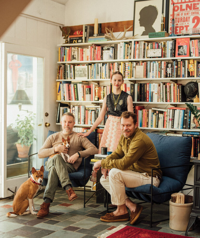 William Kinnane, John Petersen, and their daughter Riley pose with their basenjis, Emerson and Graham, in a reading nook outfitted with comfy armchairs from Camden’s DAAC Designs