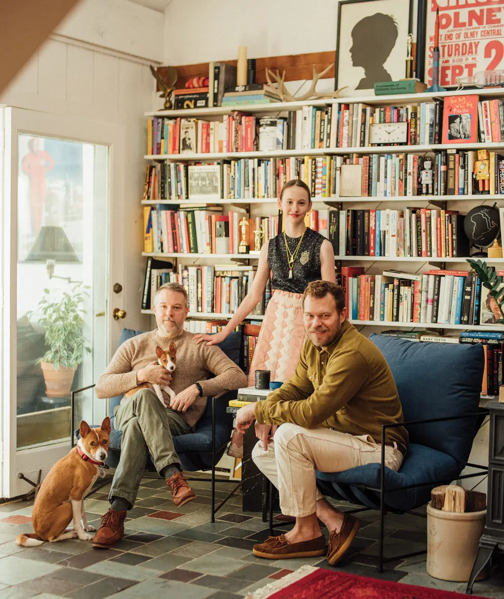 William Kinnane, John Petersen, and their daughter Riley pose with their basenjis, Emerson and Graham, in a reading nook outfitted with comfy armchairs from Camden’s DAAC Designs
