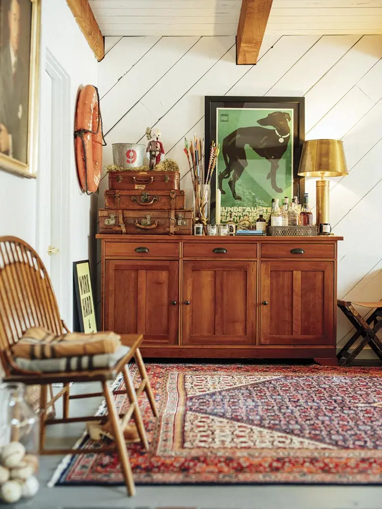 living-room bar area for guests. An RH cabinet holds liquor bottles, glasses, and collections of vintage suitcases and arrows