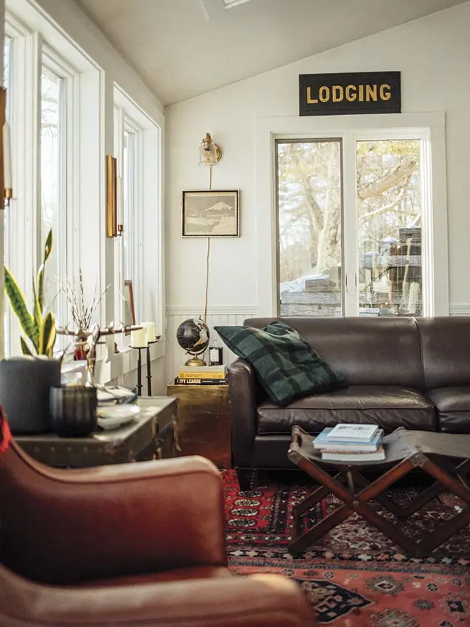 In the sunroom, John Petersen layered a patch-work of vintage carpets
over the concrete floor and brought in leather seating, an RH leather coffee table where guests can also perch, a vintage chest, a brass sconce from Rockland’s 17-90 Lighting, and brass candle sconces from Hoppe Shoppe