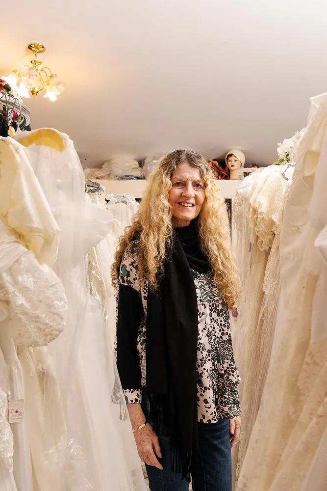 Linda Mitchell-Storer standing with her collection of vintage wedding dresses