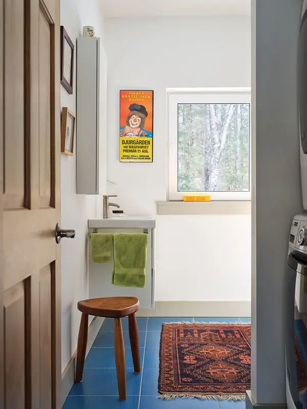 the bathroom is furnished with cobalt tile from Yarmouth’s Homestead Flooring, a ruddy carpet crafted by Negev Bedouin weavers in Israel, and a colorful poster from a Norwegian circus