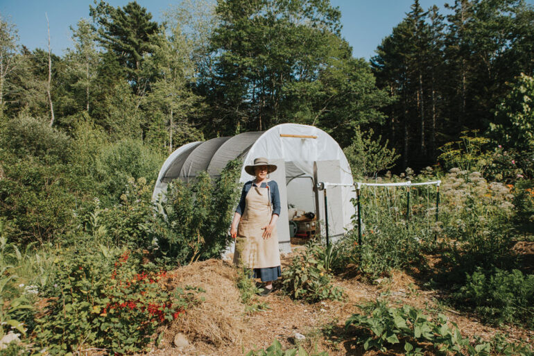 Amy Pollien stands in front of a hoop house where she keeps art supplies so she can set up her easel in the garden. At her feet is a mound of composting garden waste and other organic materials — a future vegetable bed.