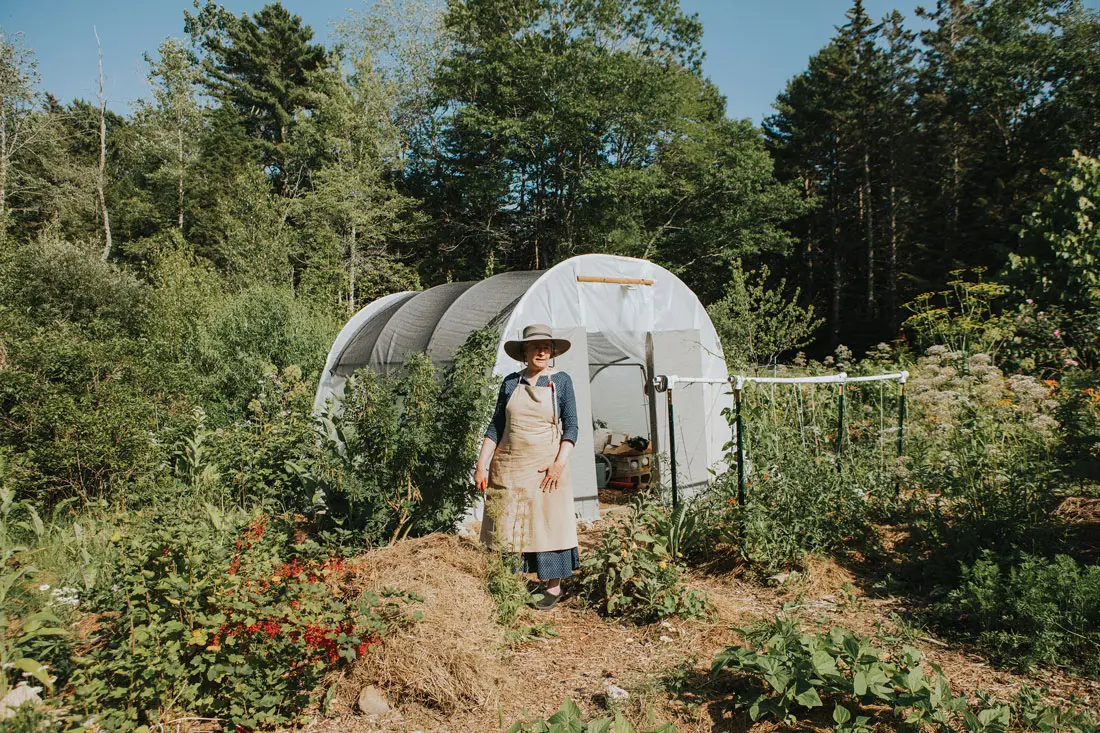 Amy Pollien stands in front of a hoop house where she keeps art supplies so she can set up her easel in the garden. At her feet is a mound of composting garden waste and other organic materials — a future vegetable bed.