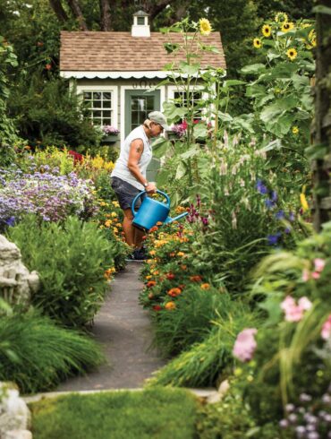 Leslie Clapp waters flowers in a cottage garden filled with herbs, vegetables, and annuals, including self-sowing sunflowers that rise 18 feet.