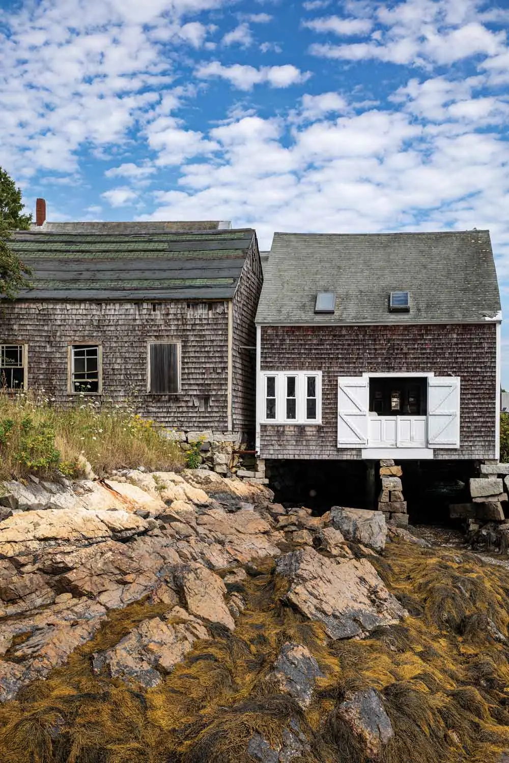 The two-room — one up, one down — cottage rests entirely on pilings; the island’s former icehouse sits behind it