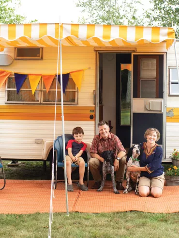 Kelly, Josh, and Abby Manahan pose with their pups, Bandito and Cowboy, and 1973 Shasta 1400 camper called Miss Marigold on their Alna property