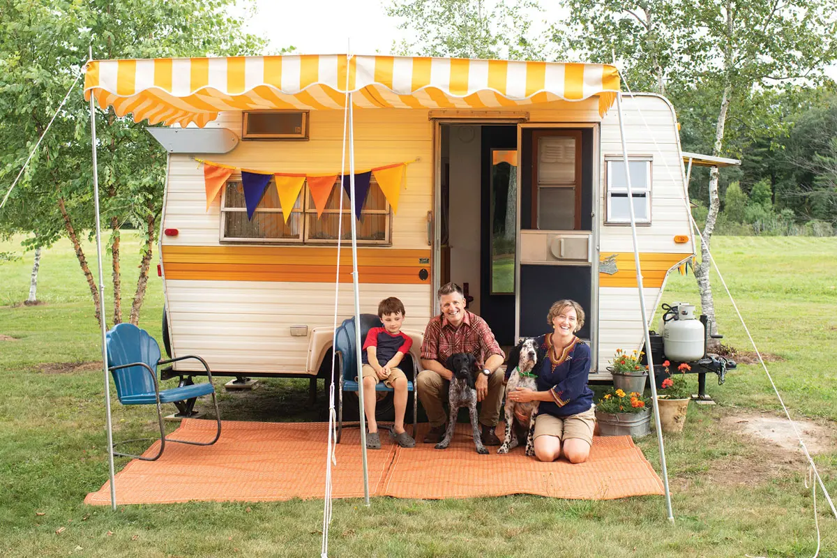 Kelly, Josh, and Abby Manahan pose with their pups, Bandito and Cowboy, and 1973 Shasta 1400 camper called Miss Marigold on their Alna property