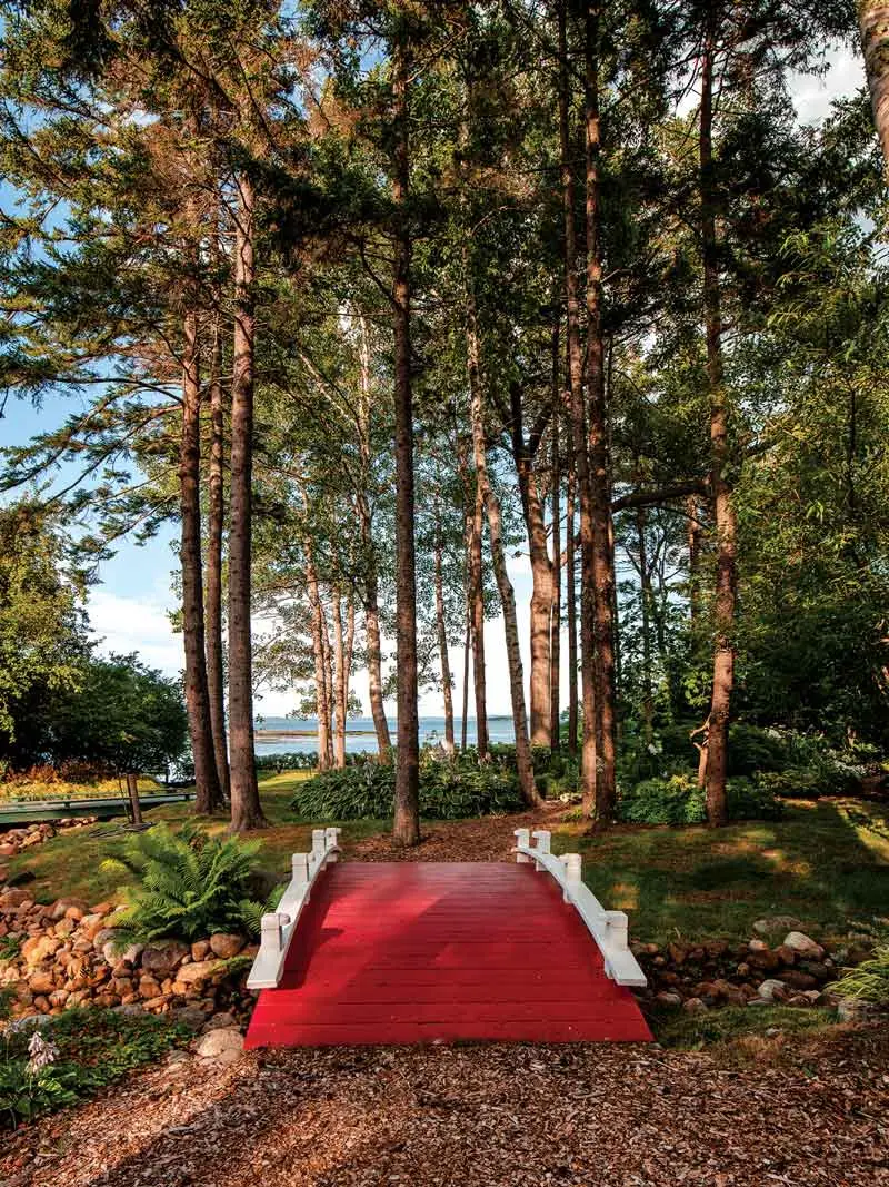 Scores of Colorful Glass Orbs Lend Continuity to This Harpswell Garden a replica of a bridge that Atkins saw in a Japanese garden arches over a stream toward Casco Bay