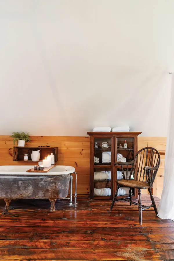 Schultz (seated) filled the former shop with antiques, such as the dining area’s 1850s cabinet from Central Maine Antique Mall, in Bangor, and 1920s chandelier. The bedroom has a rusty tub Schultz intentionally left in the rain and a sideboard from Central Maine Antique Mall chosen because “it’d had some hard living.”
