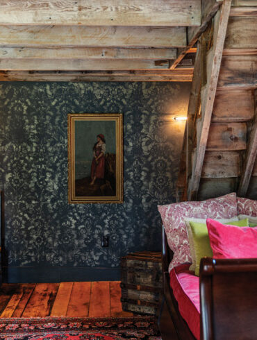 In her revamped Dover-Foxcroft barn, Brenda Schultz layered an oil painting from Brunswick’s Cabot Mill Antiques on a stenciled wall and toile and velvet pillows on a sleigh daybed.