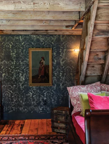 In her revamped Dover-Foxcroft barn, Brenda Schultz layered an oil painting from Brunswick’s Cabot Mill Antiques on a stenciled wall and toile and velvet pillows on a sleigh daybed.
