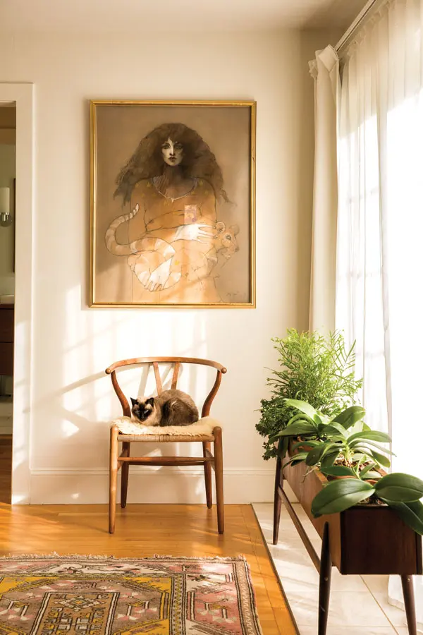In Stacey and Neil Collins’s Cumberland Foreside bedroom, an oak Hans Wegner Wishbone chair holding Siamese cat Daisy echoes the embrace in a Ramon Santiago drawing; at right is a 1950s Norwegian teak planter.