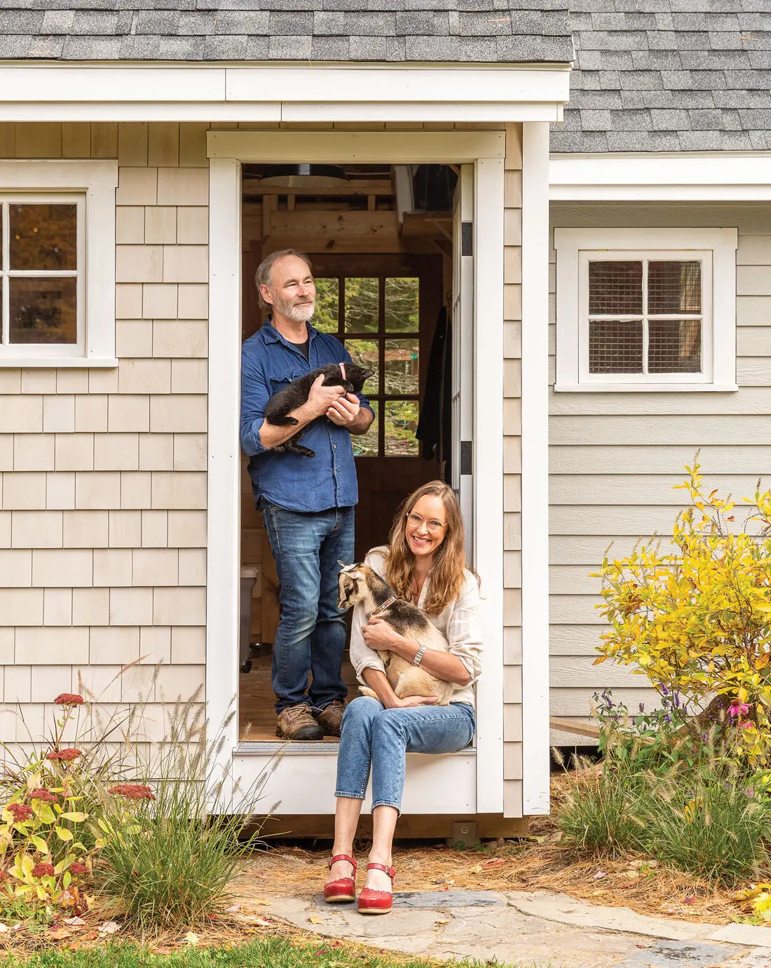 Stacey and Neil Collins pose with barn cat Fennec and Nigerian Dwarf goat Aster, in their goat barn.