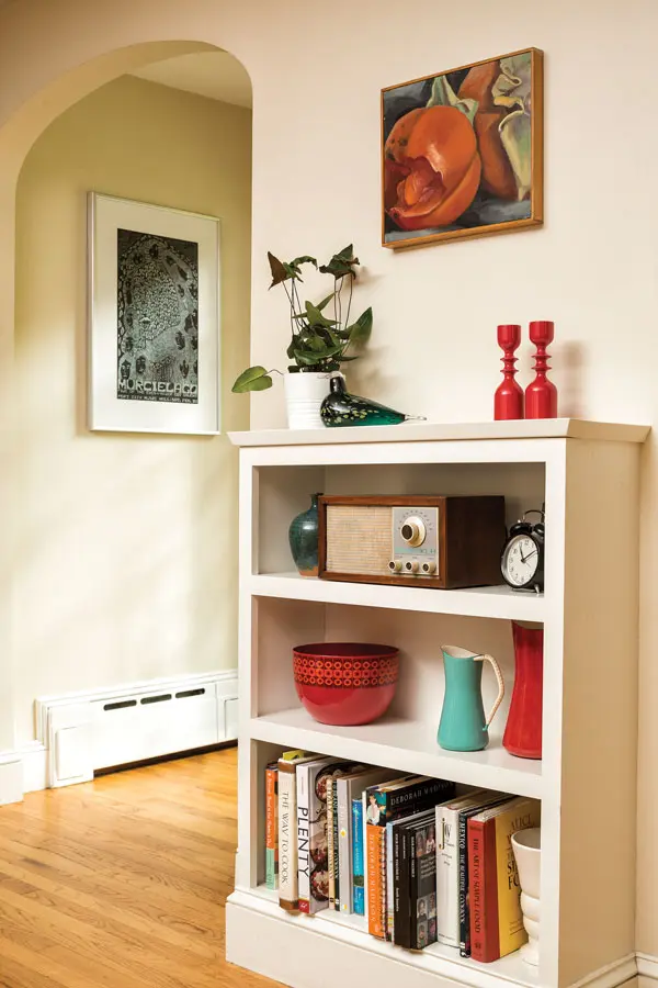 A kitchen bookshelf built by Neil displays early Dansk Kobenstyle pitchers, 1960s Danish turned candleholders, and a 1965 KLH Model Twenty-One radio. The painting is by Stacey and the poster is for Neil’s rock band.