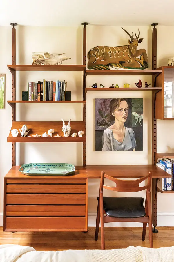 The guest room features a treasure trove of vintage gems and memorabilia, including a teak modular wall unit by Poul Cadovius framing artifacts from the family’s sailing trip, Stacey’s self-portrait, and a teak-and-leather Sawbuck chair by Hans Wegner.