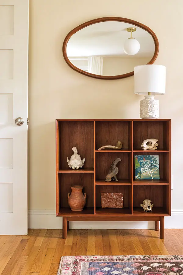 An oval teak Vildbjerg Møbelfabrik mirror offsetting a blocky teak bookshelf by Peter Hvidt and Orla Mølgaard-Nielsen filled with art and more sailing finds.