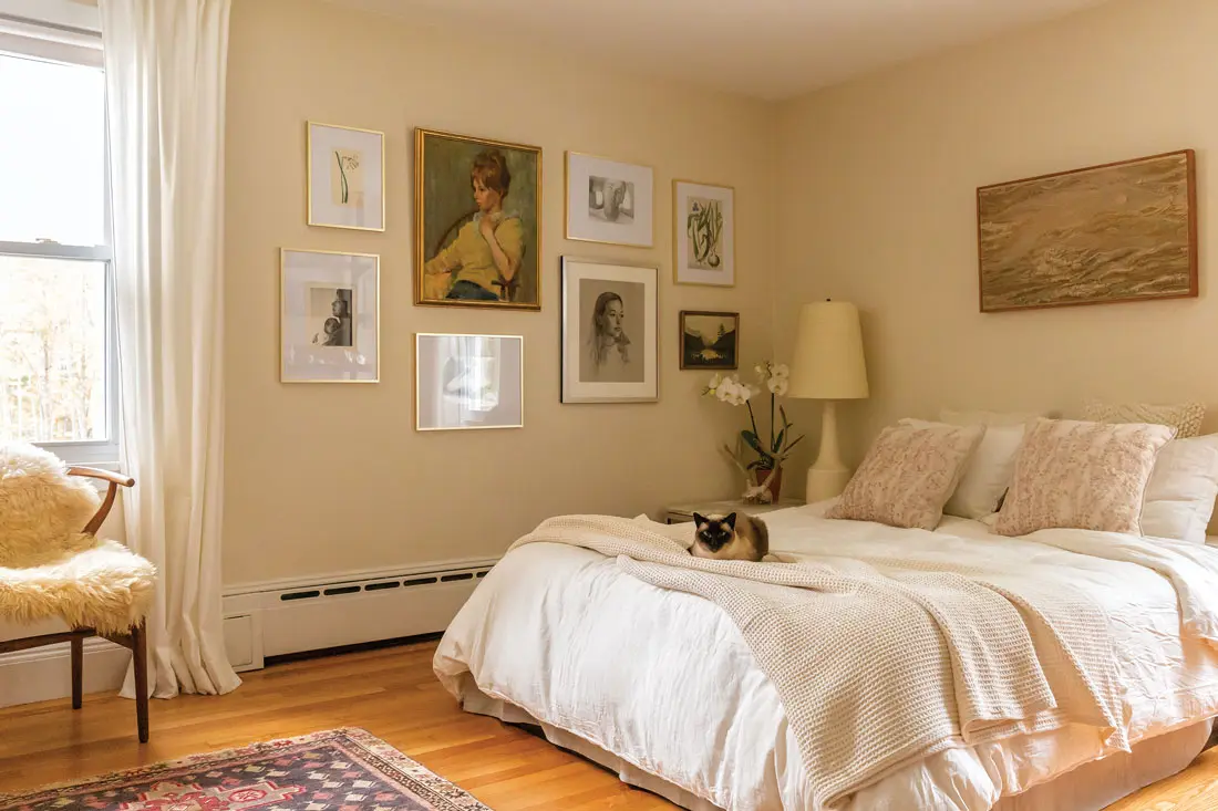 A mix of framed vintage art and family portraits, including a pencil drawing of the couple’s child, Rowan, by Neil’s mother, and a mixed-media landscape by Betty Williams. A Lotte and Gunnar Bostlund ceramic lamp, sheepskin-draped Wishbone chair, and Daisy the cat warm up the space.