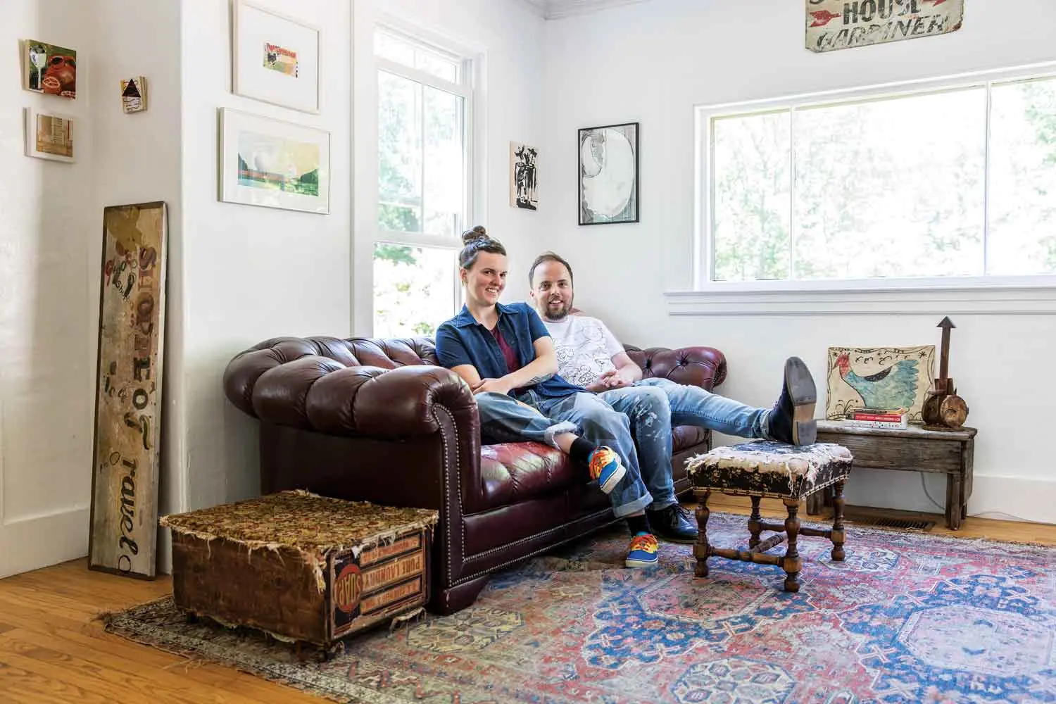 In the living room, the footrest is fraying, the rug is faded, and the end table is a soap box a previous owner outfitted with casters and a hinged, carpeted lid.
