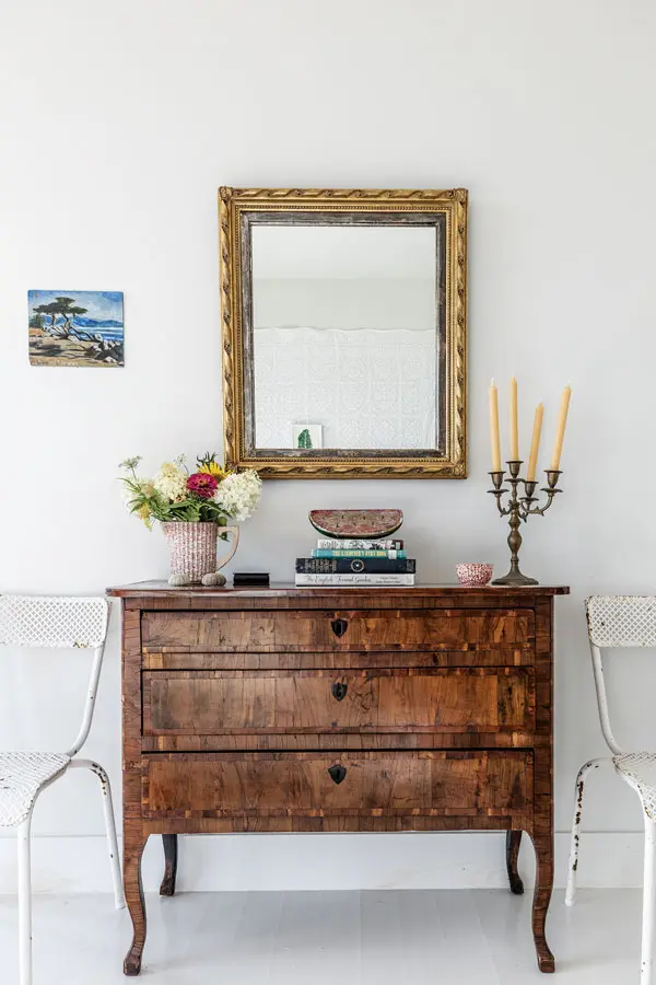 A burled-fruitwood chest and gilded mirror, flanked with 1950s French metal chairs from Marston House