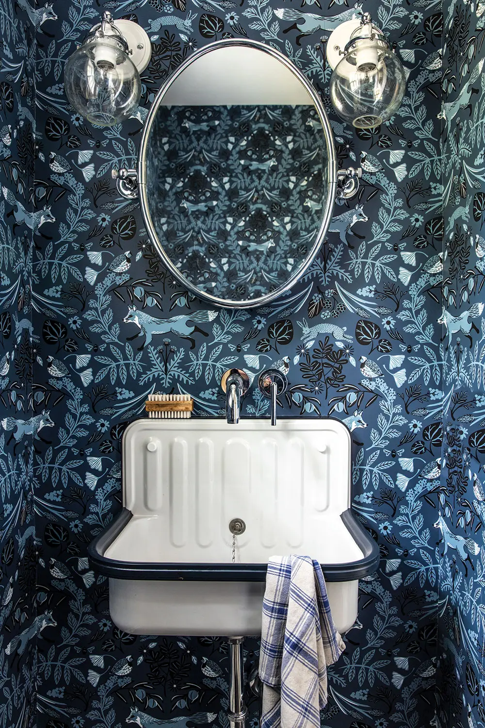 An industrial-style steel sink floats on a Hygge & West woodland scene in a powder room dreamed up by partners/sisters-in-law Heidi Lachapelle and Katie Judkins