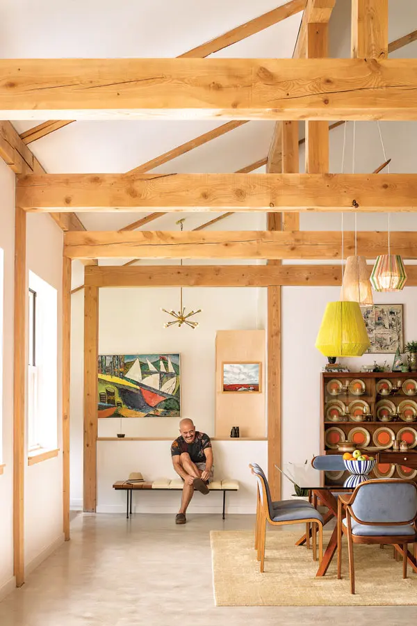 Michael Rego perches on the entryway’s vintage pine-and-vinyl bench beneath a mid-century oil and 1950s Sputnik chandelier