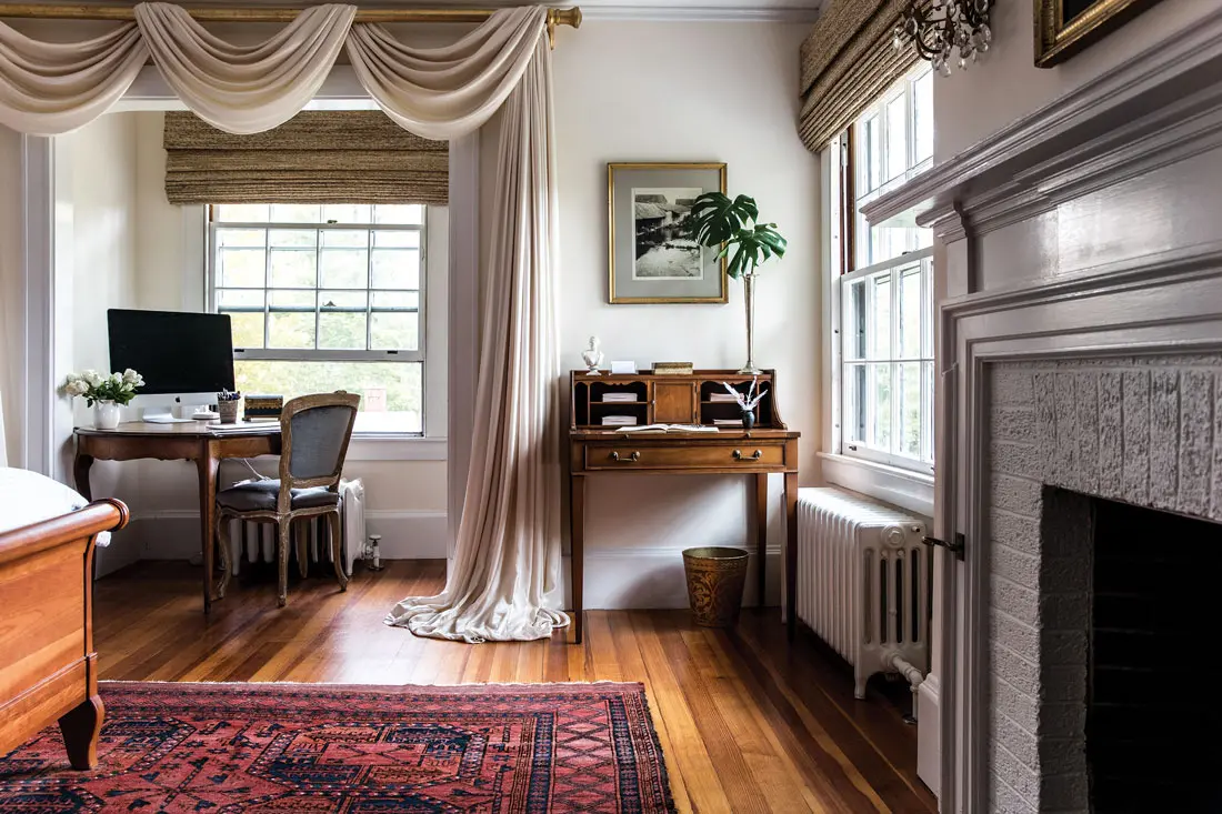 In the primary bedroom, blush-pink silk curtains blend with walls in Cream Froth by Benjamin Moore, and pick up tones in an antique rug.
