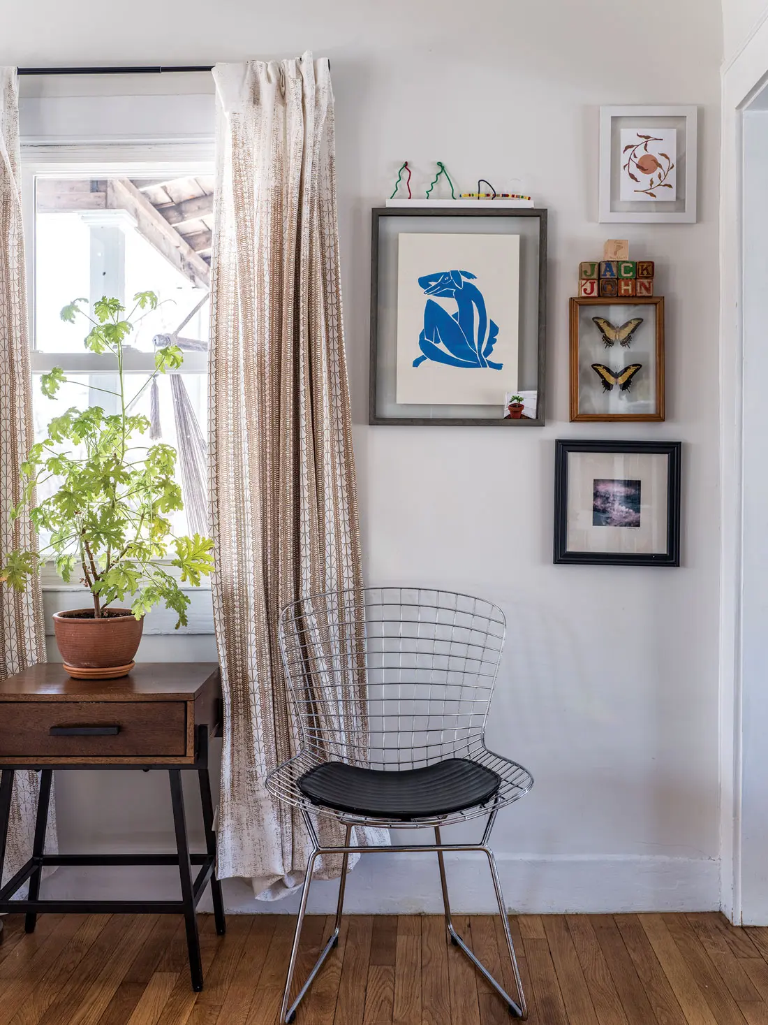A living room corner features a geranium propagated by Halchak’s mom, art by Tom Bingham, and a wire chair purchased in New York.