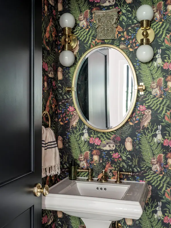 In the powder room, a Rejuvenation mirror and sconces (with bulbs from Etsy) pick up the golden tones in playful Lord Twig Hedgerow wallpaper.