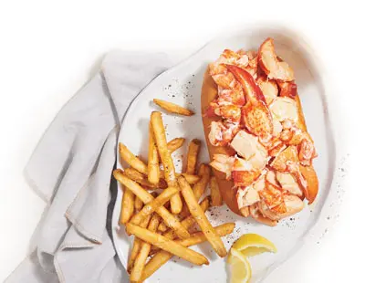 a lobster roll with french fries and lemon wedges