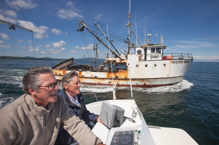 Island Institute founders Peter Ralston and Philip Conkling skipping along next to a herring seiner in Penobscot Bay.