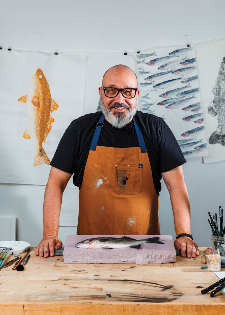 Nate Garrett in an apron with a fish print piece of art