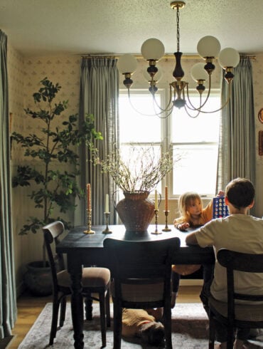 In the dining room, an espresso-colored table and secondhand chairs she stained to match provide rich counterpoints to delicate, vintage-inspired floral wallpaper, beadboard wainscoting with scalloped trim (rendered in Accessible Beige), and aqua linen curtains