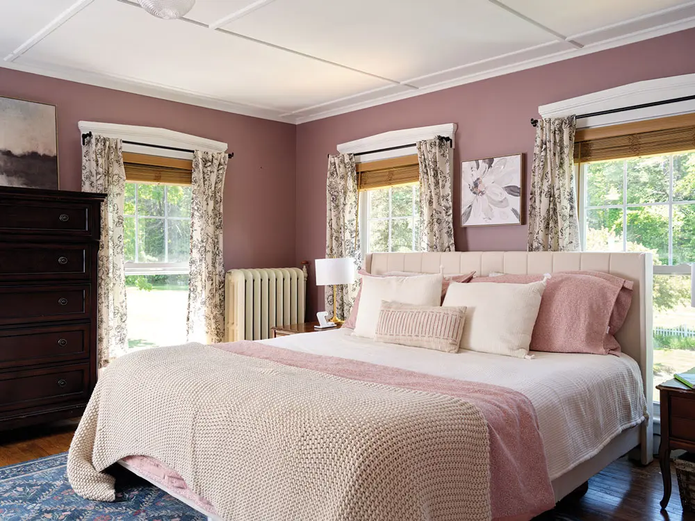 in a bedroom, mauve walls are accented with a floral rug and curtains