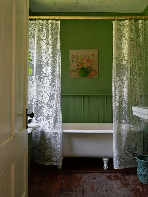 a claw-foot tub, Farrow & Ball’s Yeabridge Green on the walls, lace curtains, and a Clementine Cavanagh painting in the bathroom.