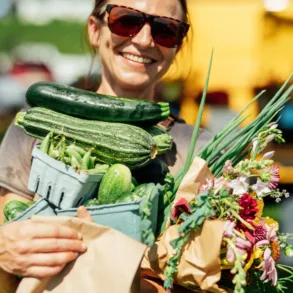 a woman in sunglasses holding all of her summer produce purchases from a Maine farmers market